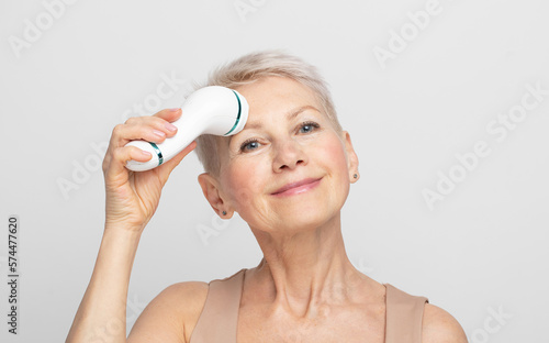 Beautiful 60s woman holding a massager in her hand and use on face. Spa technique skincare ads.