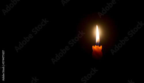 A single burning candle flame or light is glowing on a beautiful spiral orange candle on black or dark background with copy space for text on table in church for Christmas, funeral or memorial service