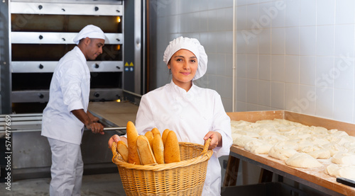 Female baker holding basket of hot baguettes in the kitchen of the bakery