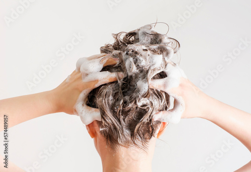 A girl washes her hair with shampoo on white background, back view.