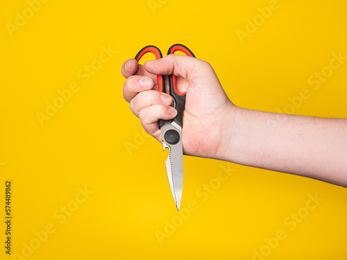 A hand holds a scissor. No face, yellow background. 