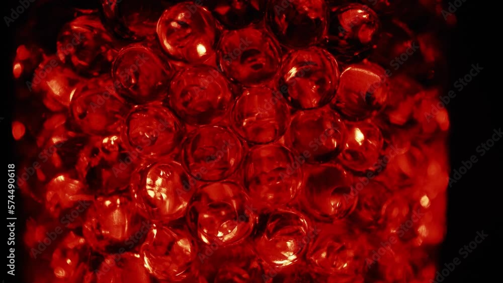 Water colored, red gel balls. Super macro bubbles slow motion. Background with hydrogel balls with glitter. The concept of cosmetology. Luminous, shiny capsules of vitamins for the face under a