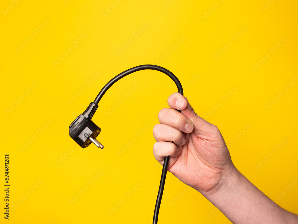 A hand holds a plug to which a black cable is attached.  No face, yellow background.
 - obrazy, fototapety, plakaty 