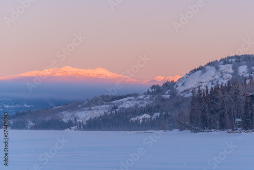 Landscape winter views in northern Canada during sunrise with pink tones on surrounding mountains and sky. Frozen lake in foreground.  © Scalia Media