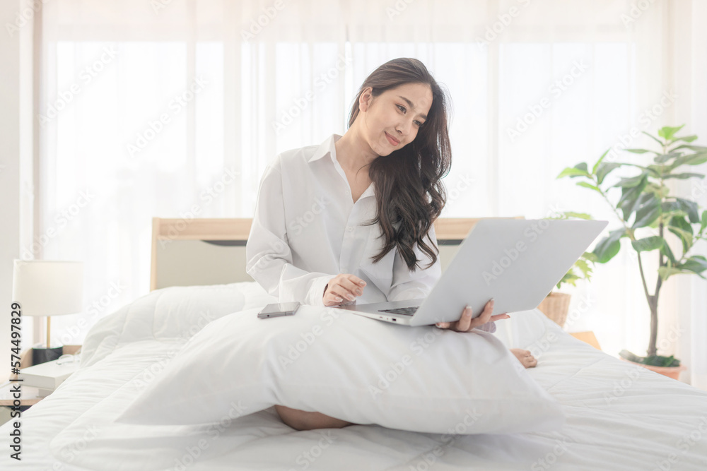 young asian woman using laptop when sitting on a bed. Smart living with ...
