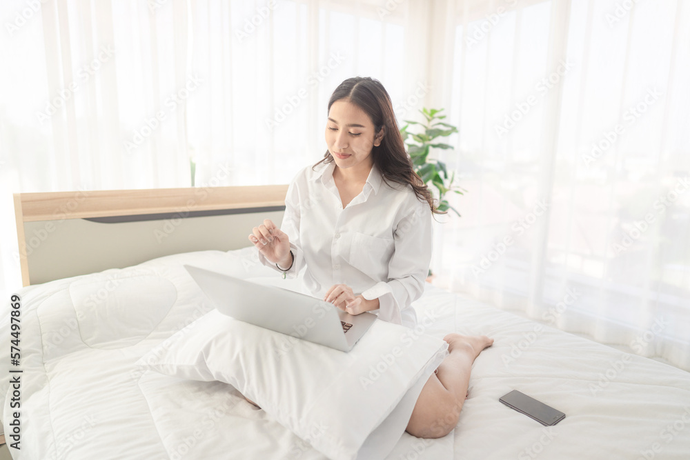 young asian woman using laptop when sitting on a bed. Smart living with ...