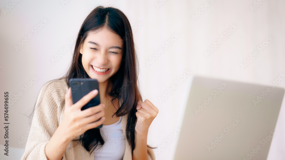 Young asian woman happy working on computer laptop and hand typing chat message on mobile smartphone at home. Video call, Online meeting Young asian woman happy working on computer laptop and hand typing chat message on mobile smartphone at home. Video call, Online meeting