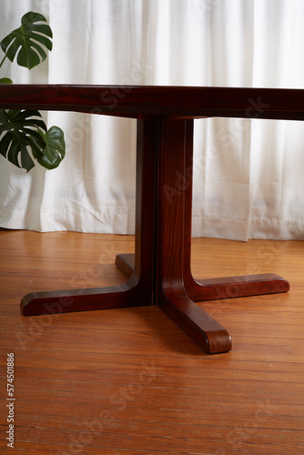 Elegant Rosewood Dining Table. Dark wooden table. Interior view with a furniture piece in front of a long white curtain with houseplants.  photo