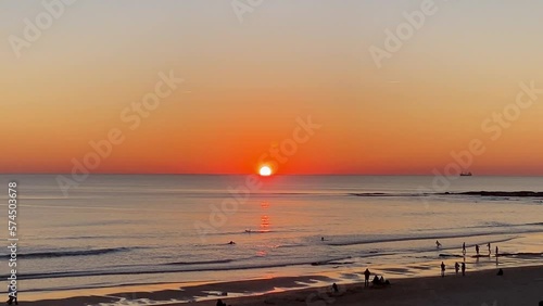 Incredible beautiful sunset sky reflections of atlantic ocean waves at Carcavelos beach, boats, ships and surfers in the water, orange teal blue tones