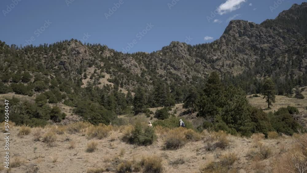 Hikers walk on trail with rugged mountain landscape in background Hikers walk on trail with rugged mountain landscape in background