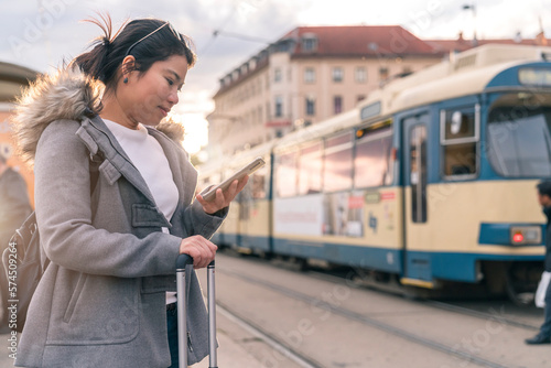 Smiling young asian woman checking schedule table of city traffic online on application using smartphone,asia woman satisfied use app for paying electric transport via cellphone waiting for tram