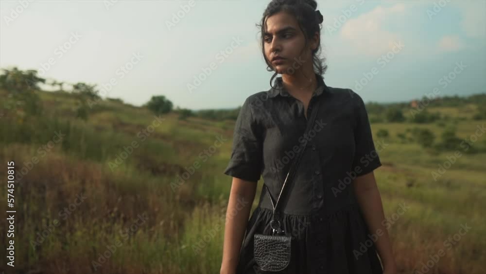 Cinematic shot of a brunette woman in a black dress posing in a field.