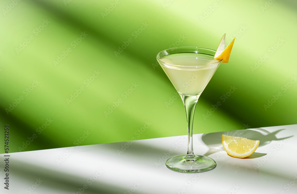 Vesper, classic alcoholic cocktail drink with dry gin, vodka, aperitif, lemon zest and ice. Light green background, hard light, shadow pattern Vesper, classic alcoholic cocktail drink with dry gin, vodka, aperitif, lemon zest and ice. Light green background, hard light, shadow pattern