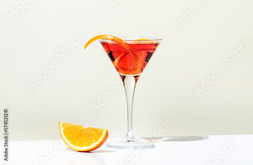 Martinez alcoholic cocktail drink with red vermouth, liqueur, orange bitter, zest and ice. Light beige background, hard light, shadow pattern. Minimalistic style photo