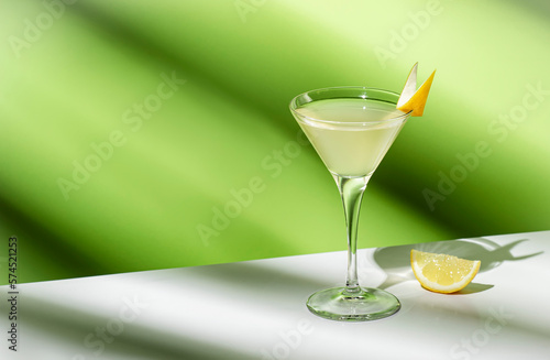 Vesper, classic alcoholic cocktail drink with dry gin, vodka, aperitif, lemon zest and ice. Light green background, hard light, shadow pattern