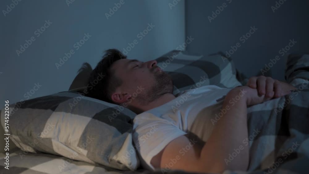 Young caucasian man spinning in bed, uncomfortable sleeping conditions. Nervous man cannot falling asleep at night, insomnia. Emotional and sleeping disorders concept. Male meeting dawn in bed. Young caucasian man spinning in bed, uncomfortable sleeping conditions. Nervous man cannot falling asleep at night, insomnia. Emotional and sleeping disorders concept. Male meeting dawn in bed.