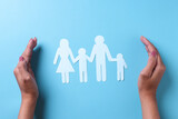 Hands covering family shape on blue background. Family insurance and medical care concept. 