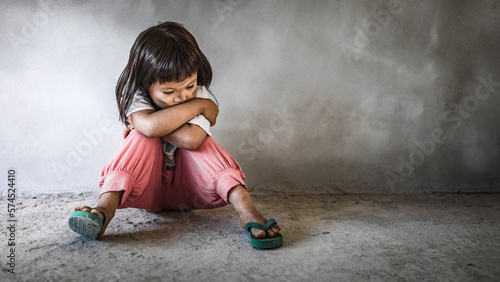 Homeless sad little child girl sitting alone on floor concrete wall background