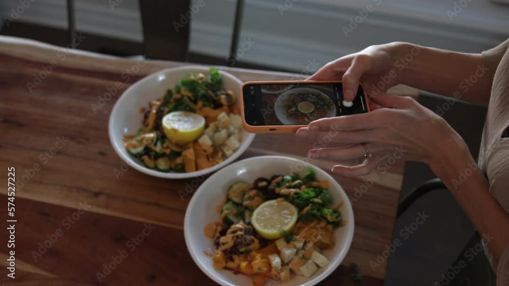 Woman takes photos of delicious vegan vegetarian meal with phone on dinner table - close up on hands and smartphone Woman takes photos of delicious vegan vegetarian meal with phone on dinner table - close up on hands and smartphone