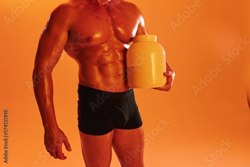 Man bodybuilder boxer with naked torso with abs holding can muscle growth pills, steroids, doping protein. Advertising, sports, active lifestyle, colored yellow light, competition, challenge concept. 