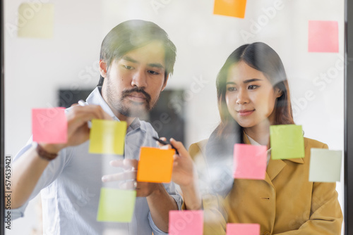 Team of Business female employee with many conflicting priorities arranging sticky notes commenting and brainstorming on work priorities colleague in a modern office.
