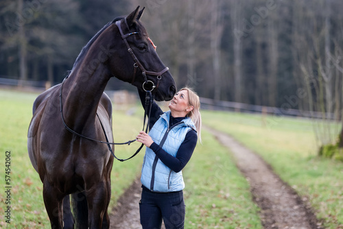 Rider stands with her horse on the dirt road and strokes the horse's forehead..