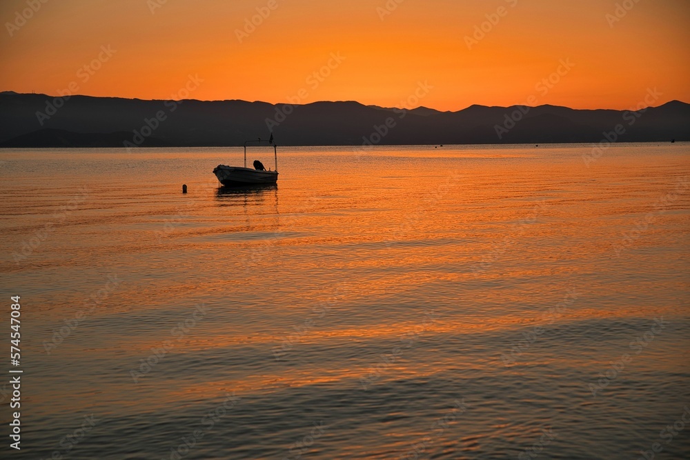 Sunset at the sea on a chain of hills, the entire sky shines in an intense gold orange and reflected in the water, on the sea a small boat. Sunset at the sea on a chain of hills, the entire sky shines in an intense gold orange and reflected in the water, on the sea a small boat.