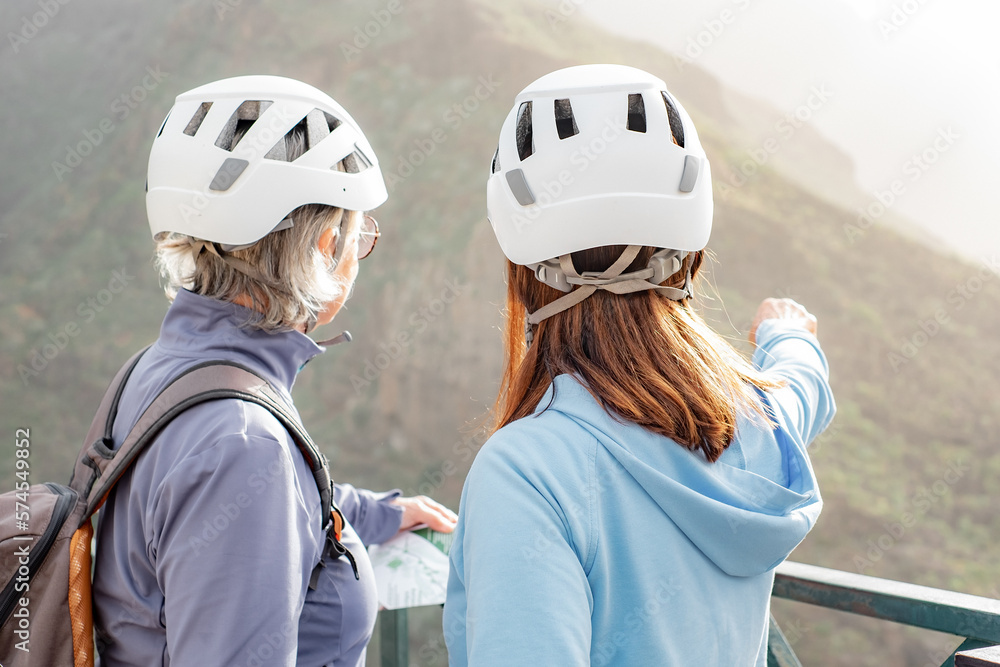 Rear view of two senior women hikers with helmets standing on top of mountain looking at landscape - mature climbing tourists enjoying holidays and healthy lifestyle - Freedom, success sport concept Rear view of two senior women hikers with helmets standing on top of mountain looking at landscape - mature climbing tourists enjoying holidays and healthy lifestyle - Freedom, success sport concept