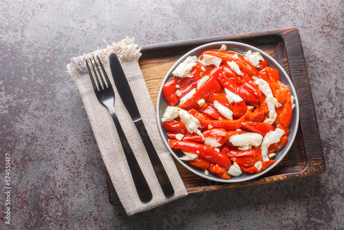 Esgarraet is a typical dish from the Valencian community in Spain it consists of grilled red pepper salad, cured cod, garlic, olive oil closeup on the plate on the wooden board. Horizontal top view photo