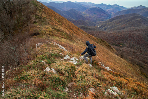 A young man with a backpack descends from the top of the mountain. A man going hiking in the Caucasus mountains. A young man on top of a mountain enjoying nature. A tourist in the mountains. 