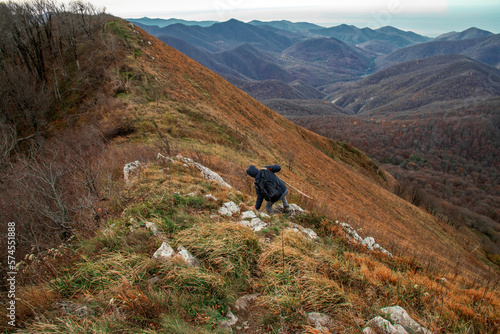 A young man with a backpack descends from the top of the mountain. A young man on top of a mountain enjoying nature. A man going hiking in the Caucasus mountains. A tourist in the mountains. 
