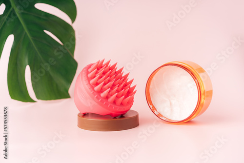 Head massager and head cream against pink background and monstera leaf. photo