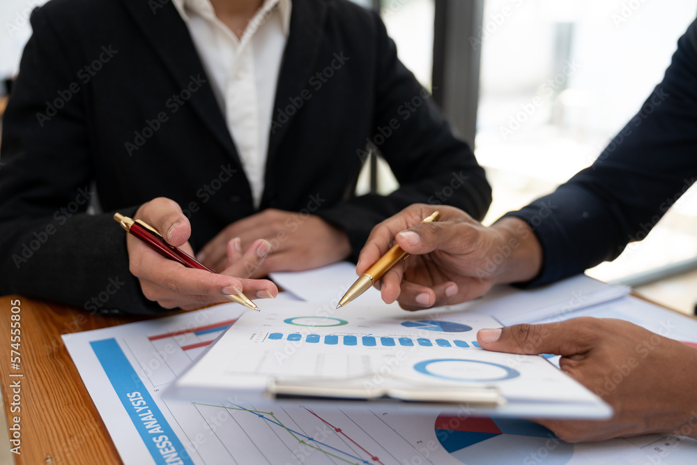 Group of Asian business people pointing to data graphs to brainstorm analyzing financial reporting situations. Calculating investment, income, tax and accounting sitting at table showing growth. Group of Asian business people pointing to data graphs to brainstorm analyzing financial reporting situations. Calculating investment, income, tax and accounting sitting at table showing growth.