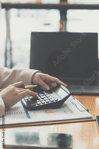Asian businesswoman analyzing data from laptop financial report situation Calculate your investment with a calculator. Income, tax and accounting data graph infographics at desk in office.