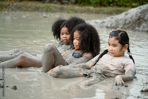 Group of happy children girl playing in wet mud puddle on summer day in rainy season