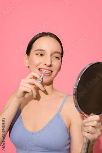 Girl with braces brushes her teeth against bright pink background