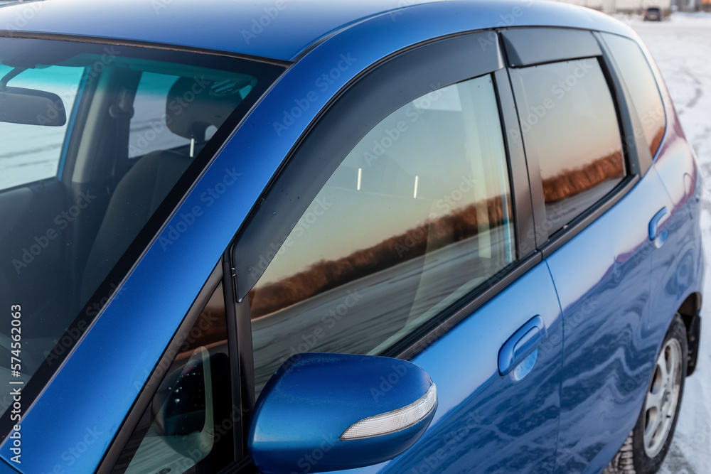Side view of a blue Japanese car in the body of a hatchback with wind visors on windows in a parking after being washed ready for sale. Side view of a blue Japanese car in the body of a hatchback with wind visors on windows in a parking after being washed ready for sale.