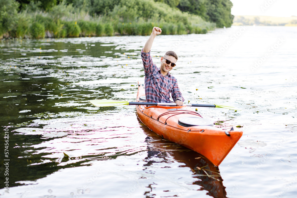 Adult caucasian man is sitting in a kayak and greetings. The concept of the water activities.