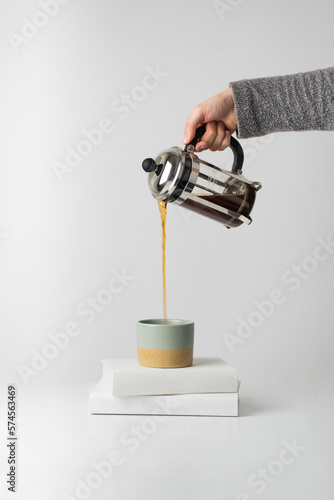Hand pouring coffee from the French press to a mug standing on books