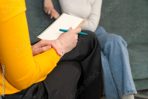 Close-up of a notebook and pen on the lap of a female consultant, psychologist, journalist, lawyer. Concept of assistance. Female psychologist holds a session with a girl on the couch in the office