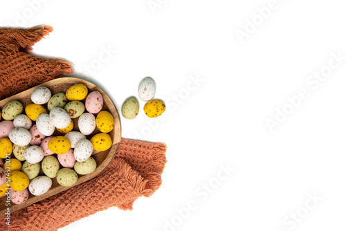 Multi-colored chocolate decorative eggs in wooden tray on a white background with brown towel. Happy Easter background. Flat lay