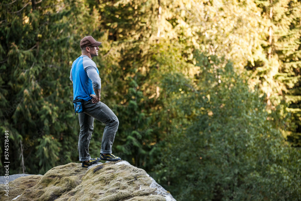 Man standing on top of rock with arms akimbo while bouldering near Elbow Lake in Fraser Valley, Harrison Mills, British Columbia, Canada Man standing on top of rock with arms akimbo while bouldering near Elbow Lake in Fraser Valley, Harrison Mills, British Columbia, Canada