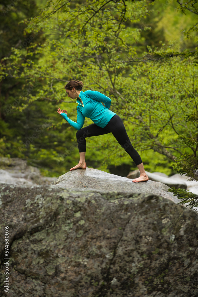 Woman practicing yoga in lunge pose on boulder in forest, Gorham, New Hampshire, USA Woman practicing yoga in lunge pose on boulder in forest, Gorham, New Hampshire, USA