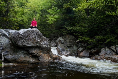 Woman practicing yoga in lotus pose on large rock in river, Gorham, New Hampshire, USA photo