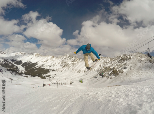 An athletic male jumping on his snowboard skillfully with an overlook of the Continental divide from Arapahoe basin ski resort. photo