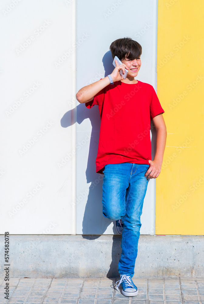 Young boy standing against a wall while talking by mobile phone Young boy standing against a wall while talking by mobile phone