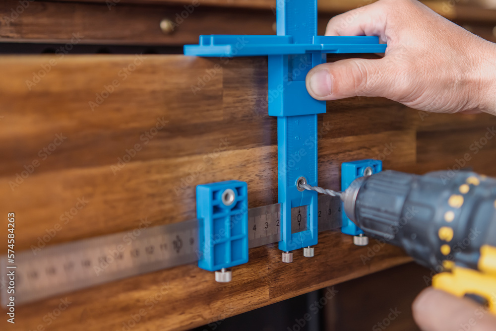 carpenter use a cabinet hardware jig adjustable punch locator drill guide sleeve for Install cabinet handles and knobs ,DIY maker and woodworking concept. selective focus carpenter use a cabinet hardware jig adjustable punch locator drill guide sleeve for Install cabinet handles and knobs ,DIY maker and woodworking concept. selective focus