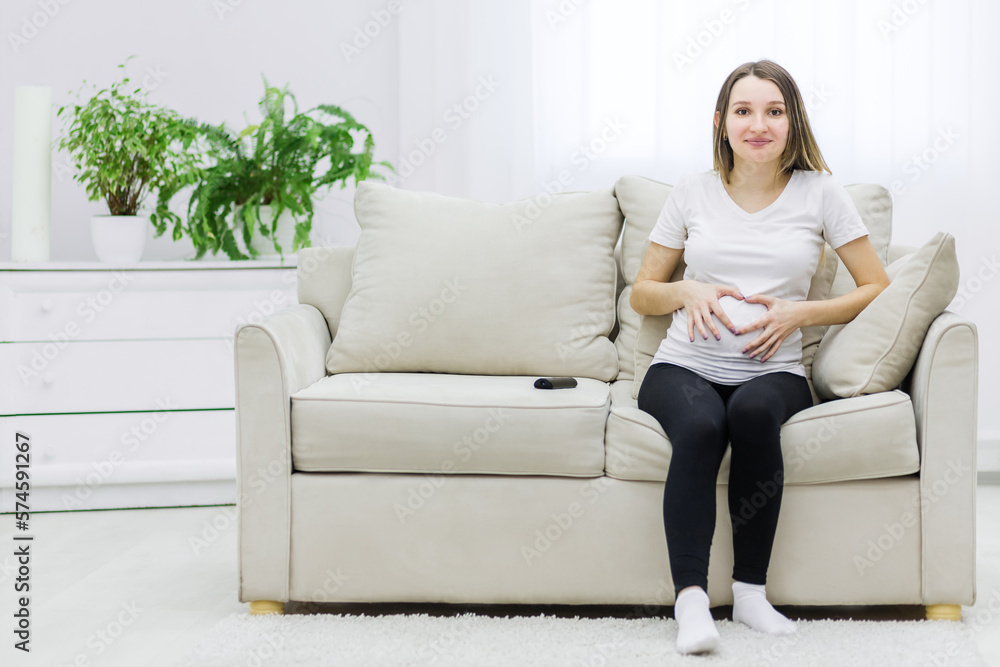 Obraz premium Photo of cute pregnant woman showing a heart with her fingers on stomach.