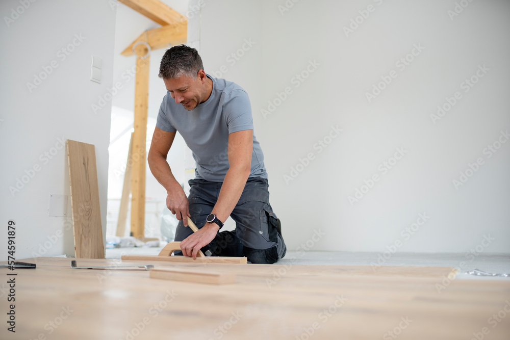 Middle aged man with grey hair and grey shirt laying parquet floor in new loft, house Middle aged man with grey hair and grey shirt laying parquet floor in new loft, house