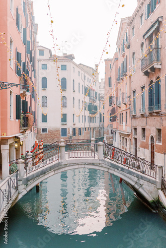 A canal runs through the canyons of houses in Venice, a beautiful bridge connects the sides. The water glitters turquoise and the sun is reflected in the brick facades of the houses. © Miriam